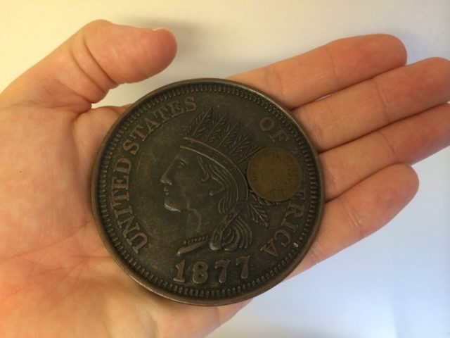 Here I hold a large Indian Head penny replica against a regular-sized Indian Head cent. 